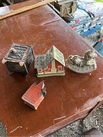 Overview of all four banks: a black safe-shaped bank, red and green house bank, red church bank, and silver plated rocking horse