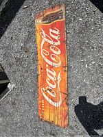 Full view of long rectangular antique Coca-Cola tin sign with red background and white Coca-Cola script logo, showing significant wear and rust.