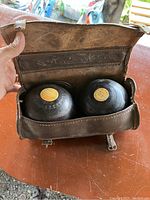 Open leather case showing two black wooden bowling balls with light-colored wood inlays on top inside the case.