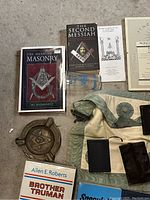 Overview of books, apron, metal dish, glass tumbler, certificate and notebooks on concrete floor