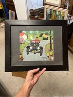 Framed print held in hand showing full artwork including black frame and matting.