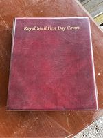 Closed maroon binder album with gold embossed 'Royal Mail First Day Covers' text on front cover showing slight wear.