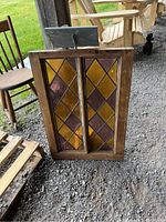 Front view of antique stained glass window showing amber and purple diamond-patterned panes within wooden frame.