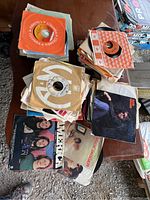 Overview of multiple stacks of 45 RPM vinyl records in colorful original paper sleeves from various record labels, showing some wear from age and use.