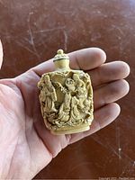 Front side of the carved snuff bottle showing three figures in traditional attire surrounded by natural motifs.