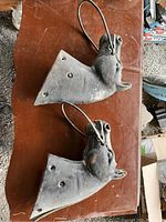 Two cast iron horse head tethers placed side by side on a wooden surface showing front top view with rings through their mouths.