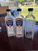 Front view of three vintage embalming bottles, two with intact labels reading Dominion Peerless Cavity Fluid and one clear embossed bottle without label.