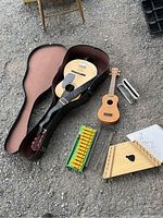 Photo showing the guitar in its case, ukulele, xylophone, harmonica case, and zither with punched music sheet arranged on the ground.