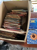 Box filled with a large quantity of vintage 45 RPM records in paper sleeves stacked inside a cardboard box