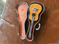 Miniature vintage guitar in original hard case with red plush lining, showing guitar body and neck inside case.