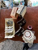 Two View-Master viewers, original boxes, white reel holder on wooden table with various reels and slides