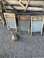 Three wooden washboards leaning against a wood wall with a clothes washing plunger in front on ground