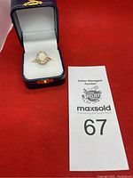 Ring displayed in navy blue jewelry box with white interior alongside auction lot card