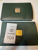 Two green leatherette cases containing coin sets from Royal Canadian Mint, one with silver emblem and one with gold emblem.