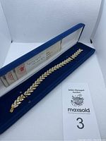 Full view of the gold-tone bracelet in blue velvet-lined case with documentation visible.