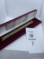 Full view of gold tone bracelet with blue stones in burgundy box with certificate and auction tag.