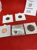 Overview of all five coins, four in white cardboard holders and one ancient Greek coin in a plastic protective case.