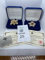 Two floral brooches in blue velvet boxes with certificates of authenticity including auction tag showing lot number 25.