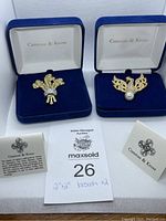 Two blue velvet jewelry boxes displaying brooches, with Camrose & Kross branding visible inside lid and informational cards included