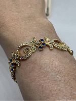 Bracelet on wrist showing gold-tone links decorated with blue stones and clear rhinestones.