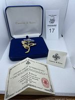 Flower brooch displayed in its original blue velvet box with Camrose & Kross branding and certificate of authenticity from Jackie Bouvier Kennedy collection.