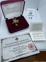 Gold-tone girl brooch with rhinestone details in red velvet presentation box labeled Camrose & Kross; manufacturer's certificate and informational card partially visible