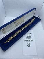 Photo of JBK gold coloured bracelet with green stones displayed in blue velvet case alongside certificate and auction card