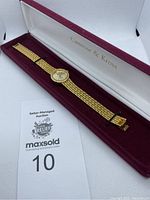 Gold colored Jackie Kennedy-style Camrose & Kross quartz wristwatch with linked bracelet, displayed inside branded burgundy and white box.