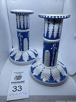 Pair of blue and white ceramic candlesticks with raised leaf and floral design, shown side by side.