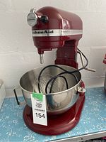 Front view of red mixer with stainless steel bowl and attachments inside