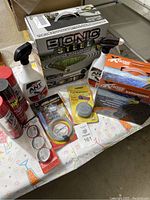 Items on table showing garden hose box, insect sprays, drain snake tool, and small insect bait containers.