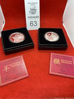 Two Silver Shield silver proof medallions displayed in black cases with red certificates in front, set against a red background.