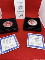 Two silver medallions in black display cases with certificates of authenticity under each, showing both medallions and certificates clearly.