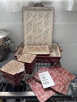 Full view of the baking dishes in cream with burgundy floral lace pattern on ceramic, showing multiple sizes and shapes along with three fabric trivets.