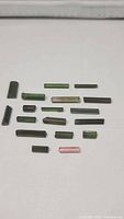 Photo of assorted full terminated rough tourmaline crystals, various shades of green, brown-green, and a pink crystal, on white background showing size and shape variety.