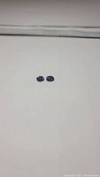 Photo of two small oval cut deep purple Iolite gemstones laid on a white background, showing their size and color under light.