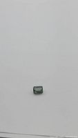 Emerald-cut green Ceylon sapphire flat on white background, showing overall shape and color.