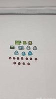 Photo showing all 21 faceted stones laid out flat in rows by type and color on a white background