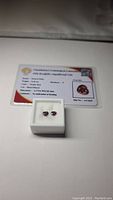 Two heart-shaped rubies in white display box with certification card in background