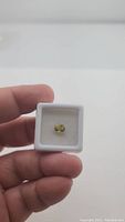 Oval cut bright yellow sapphire in white cushioned display box held by hand, shown from front view.