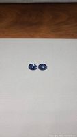 Two oval blue gemstones side by side on a neutral background, full view