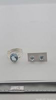 Photo showing the 6ct oval sky blue topaz ring and pair of 3ct round sky blue topaz stud earrings on gray background.