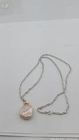 Full view of the necklace showing the baroque pearl pendant and silver chain against a white background.