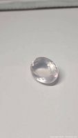 Oval cut rose quartz gemstone on a white background, showing light pink color and faceting details.