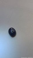 Blue star sapphire oval cabochon gemstone shown on flat surface under ambient light, visible 6-ray star effect under directional lighting.