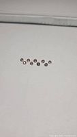 Photo showing 10 round faceted padparadscha colored sapphires with purple undertone laid out in a line on a white background.