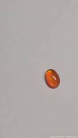 Photo of single oval cabochon Fanta orange fire opal gemstone showing vibrant orange color and play of color on plain background.