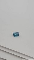 Oval-shaped lagoon blue zircon gemstone shown close-up on white background highlighting cut and clarity.