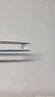 Oval cut light ice blue Ceylon sapphire held by tweezers on white background, showing clarity and color details