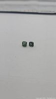 Full view of the two small square emerald cut green sapphires on a white background for color and clarity display.